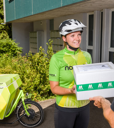 Zufriedene Velokurierin von notime übergibt Paket an einen Kunden.